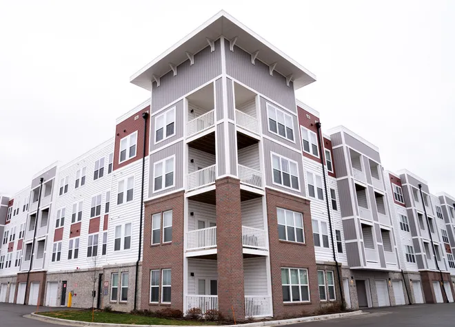 A four-story apartment building with a brick-and-siding exterior, stacked balconies, and ground-floor garages, viewed from the corner under an overcast sky.